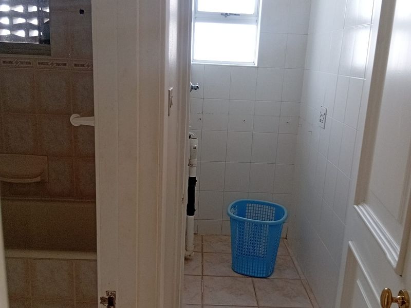 A small, tiled bathroom featuring a window and exposed plumbing, currently vacant and in need of cosmetic updates.