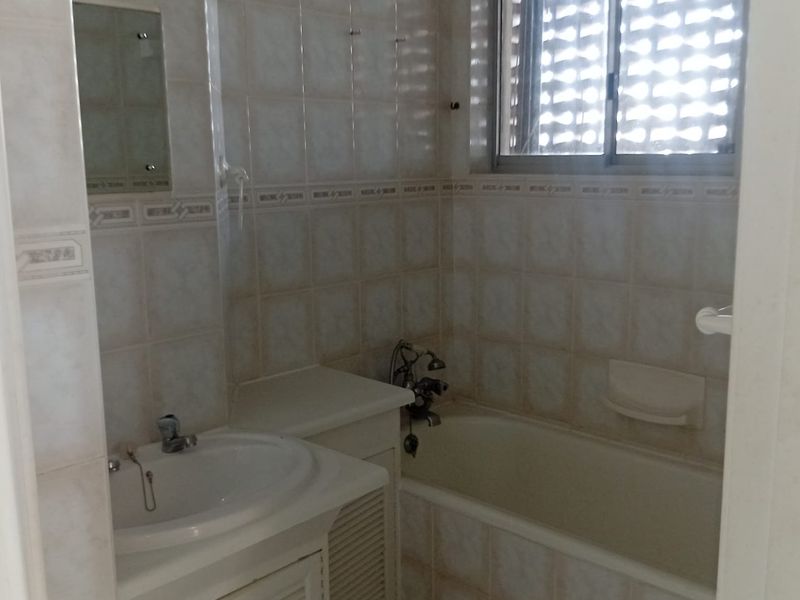 A compact bathroom featuring a built-in vanity, ceramic basin, and a bathtub with tiled wall finishes throughout.