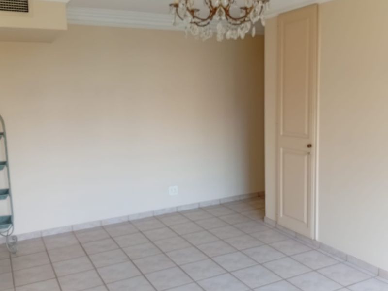 An empty living room featuring tiled flooring, crown molding, and a classic crystal chandelier, providing a neutral canvas for interior design.