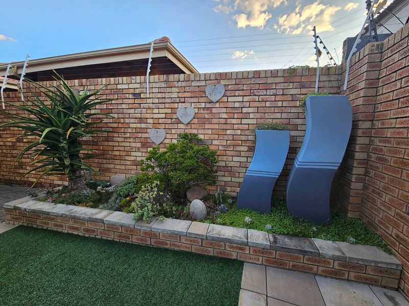 A well-maintained garden area featuring a face brick boundary wall with integrated electric fencing, a raised brick planter bed, and artificial lawn.