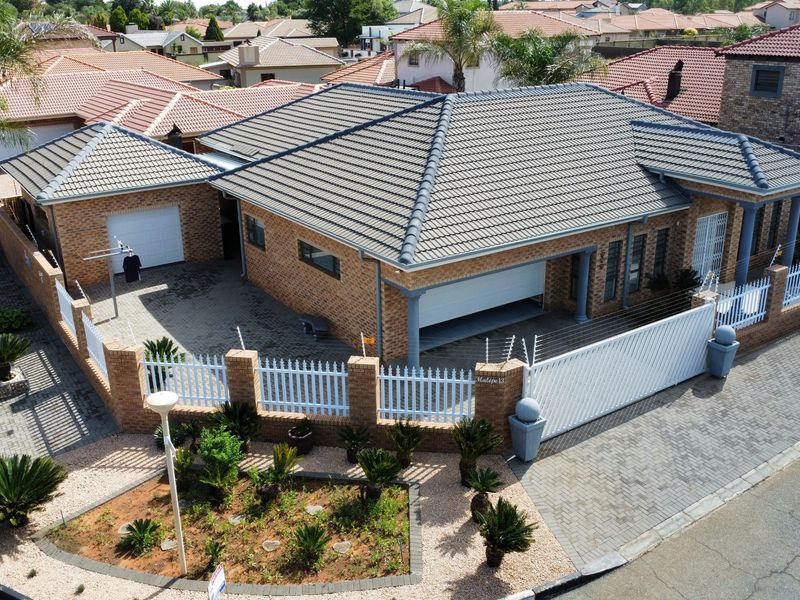 Aerial view of a well-maintained brick house featuring a tiled roof, paved driveway, secure boundary wall with electric fencing, and an automated garage.