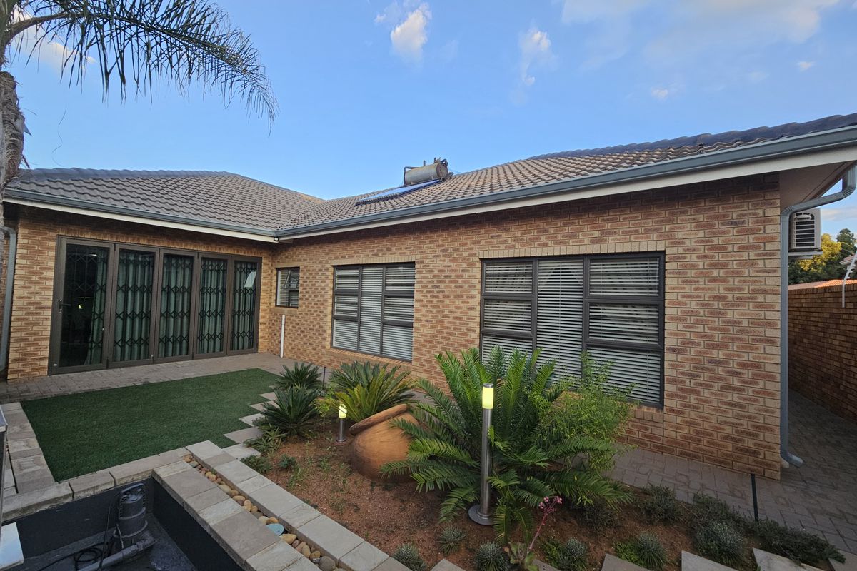 Rear exterior view featuring a brick facade, tiled roof with solar geyser, aluminium windows with security gates, and a landscaped garden with a water feature.