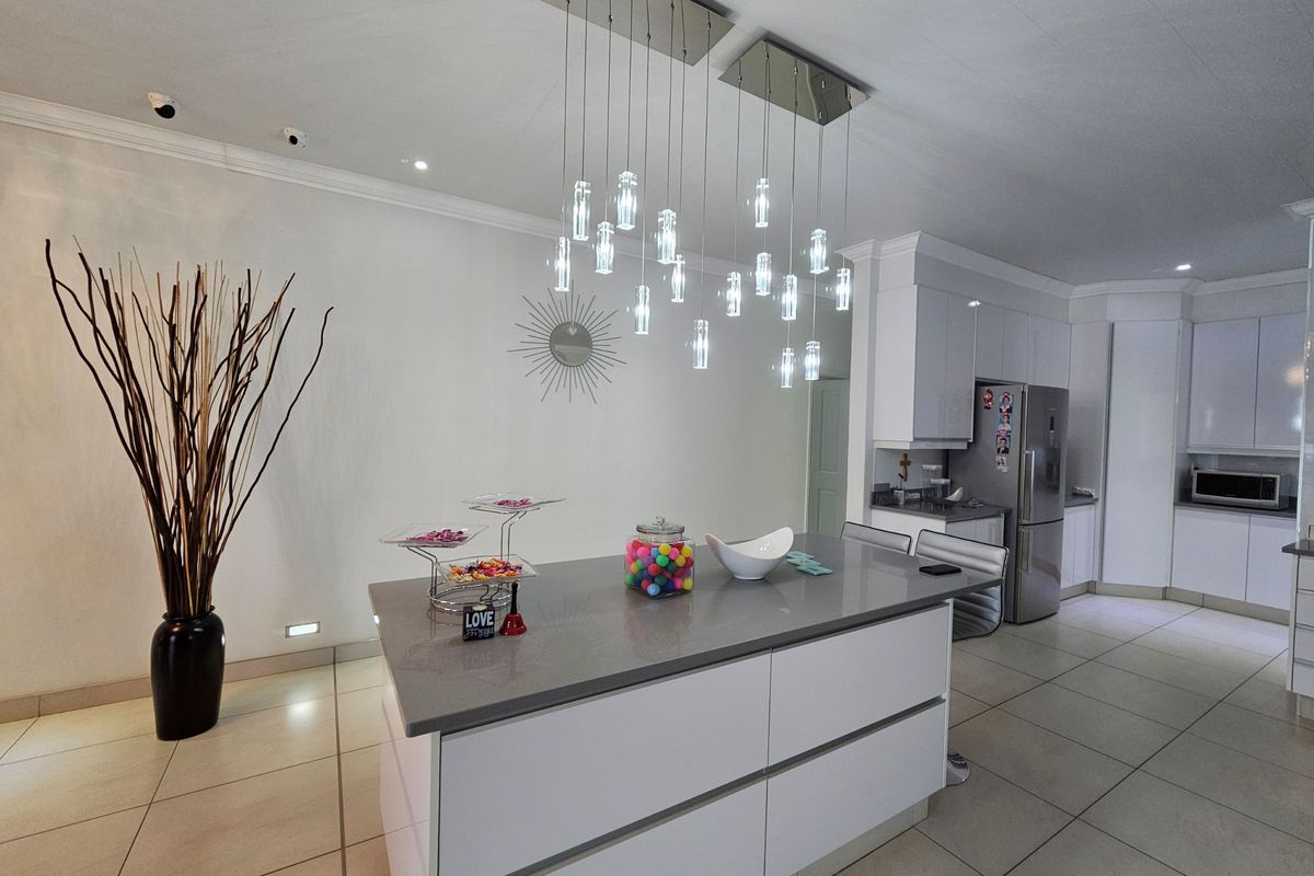 Modern kitchen featuring a central island with quartz countertops, sleek white cabinetry, and contemporary pendant lighting, set against neutral tiled flooring.