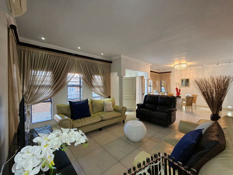 Spacious open-plan living and dining area featuring neutral tiled flooring, recessed downlighting, and large windows with fitted blinds.