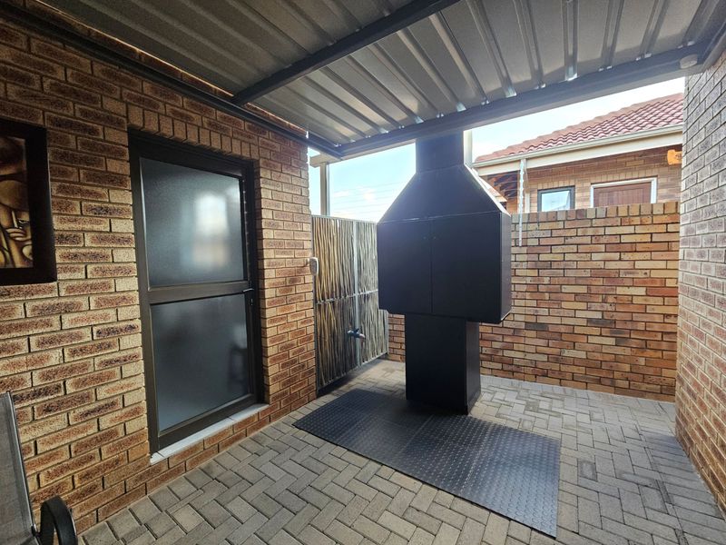 Covered outdoor patio area featuring a built-in braai, facebrick walls, and durable paved flooring, ideal for outdoor entertaining.