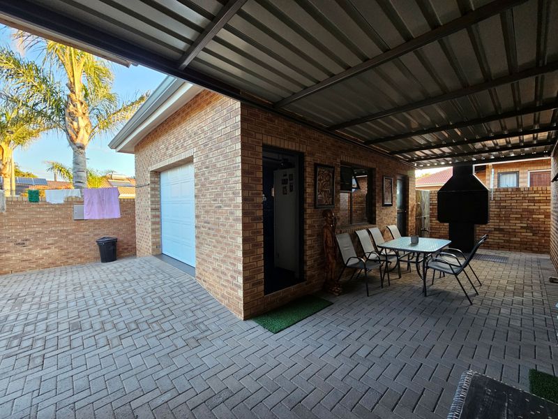 Covered outdoor patio area featuring brick construction, paved flooring, and a built-in braai, providing a functional space for outdoor entertaining.