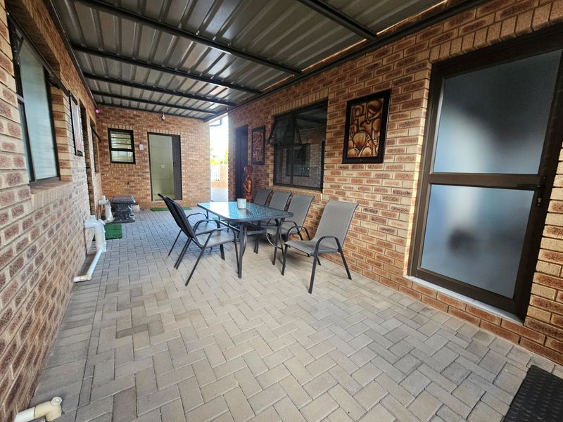 A covered outdoor patio area featuring face-brick walls, paved flooring, and a corrugated metal roof, providing a functional space for outdoor dining.