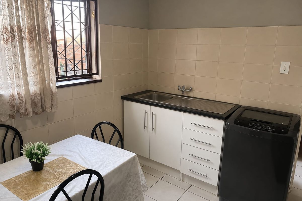 A functional kitchen area featuring built-in cabinetry, a stainless steel sink, tiled splashbacks, and security bars on the window.