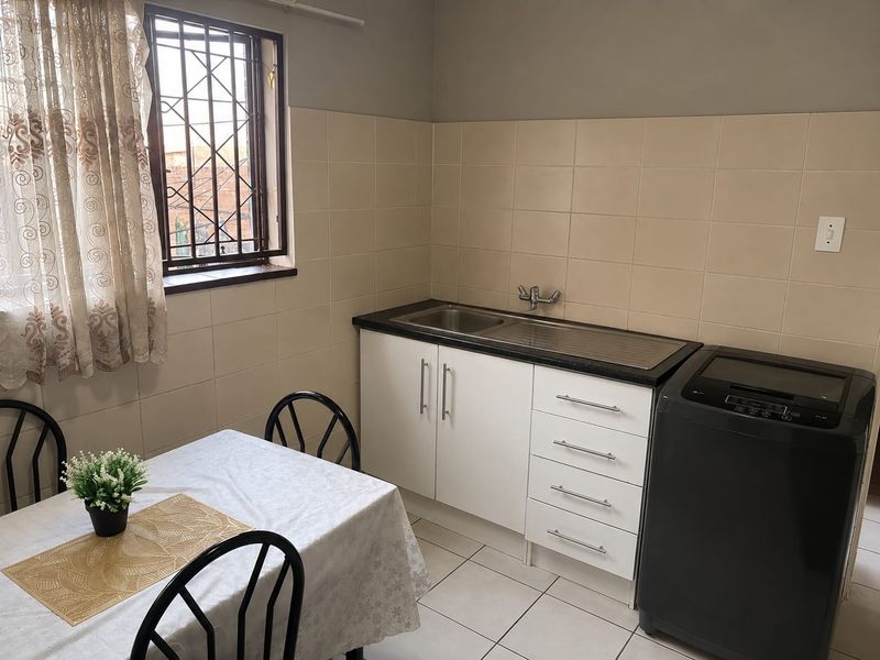 A functional kitchen area featuring built-in cabinetry, a stainless steel sink, tiled splashbacks, and security bars on the window.