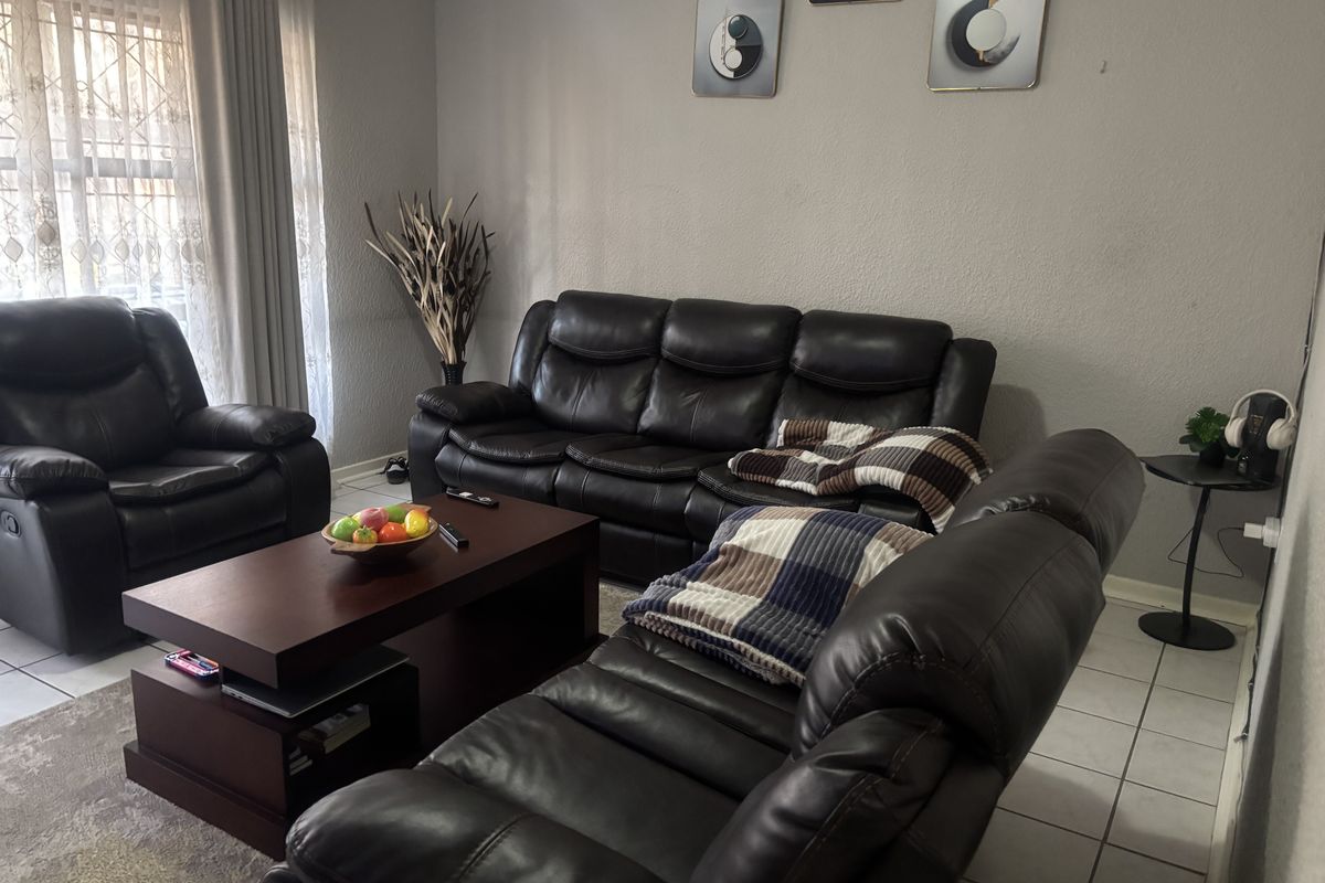 A comfortable living room featuring tiled flooring and large windows with curtain tracks, providing a functional and well-lit space.