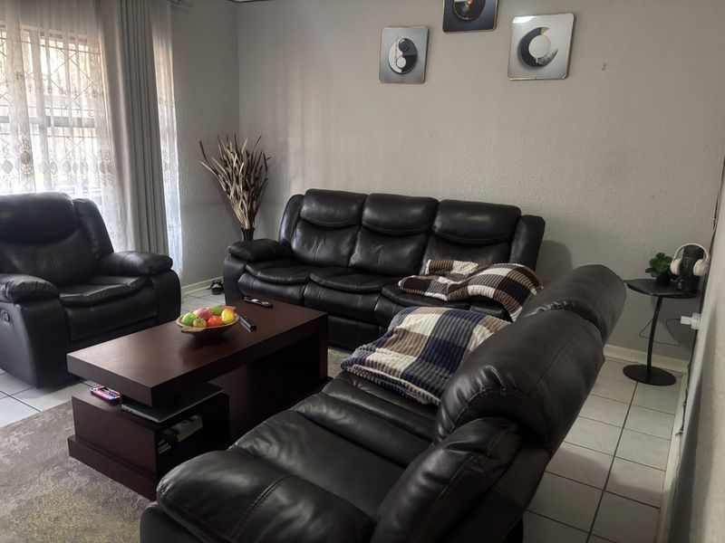 A comfortable living room featuring tiled flooring and large windows with curtain tracks, providing a functional and well-lit space.