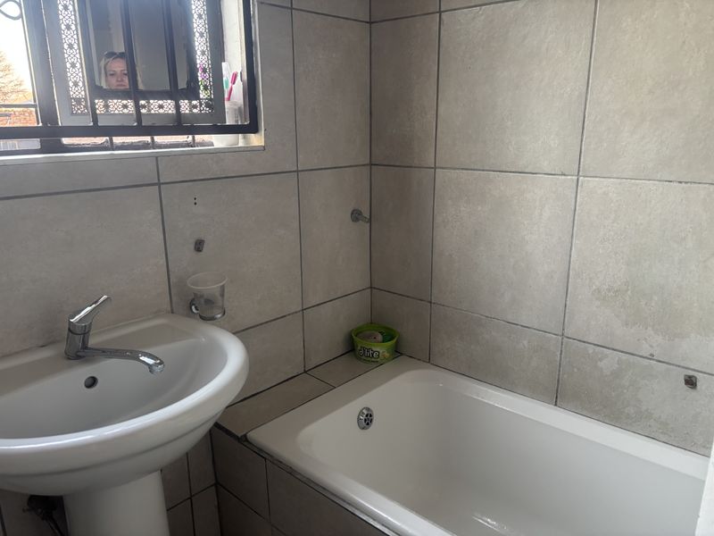 A functional bathroom featuring a pedestal basin, chrome mixer tap, and a built-in bathtub with neutral ceramic wall tiling.