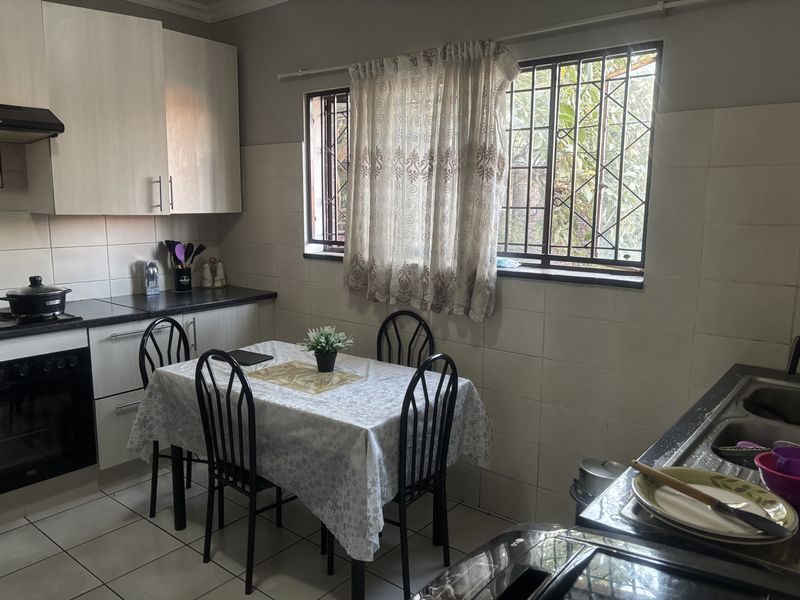 Functional kitchen featuring built-in cabinetry, laminate countertops, integrated oven, extractor fan, and tiled splashbacks with a window providing natural light.