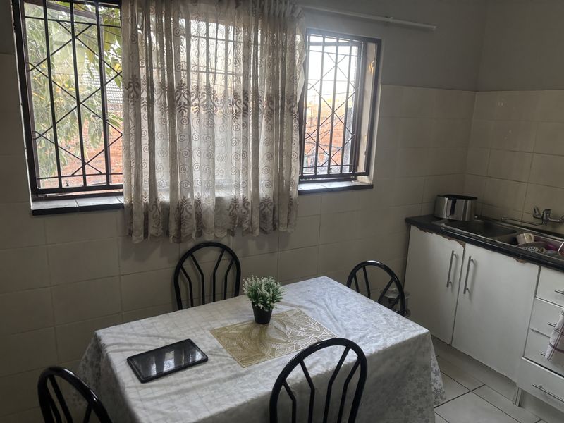 A functional kitchen area featuring tiled walls, built-in cabinetry, and a stainless steel sink, with security bars installed on the windows.