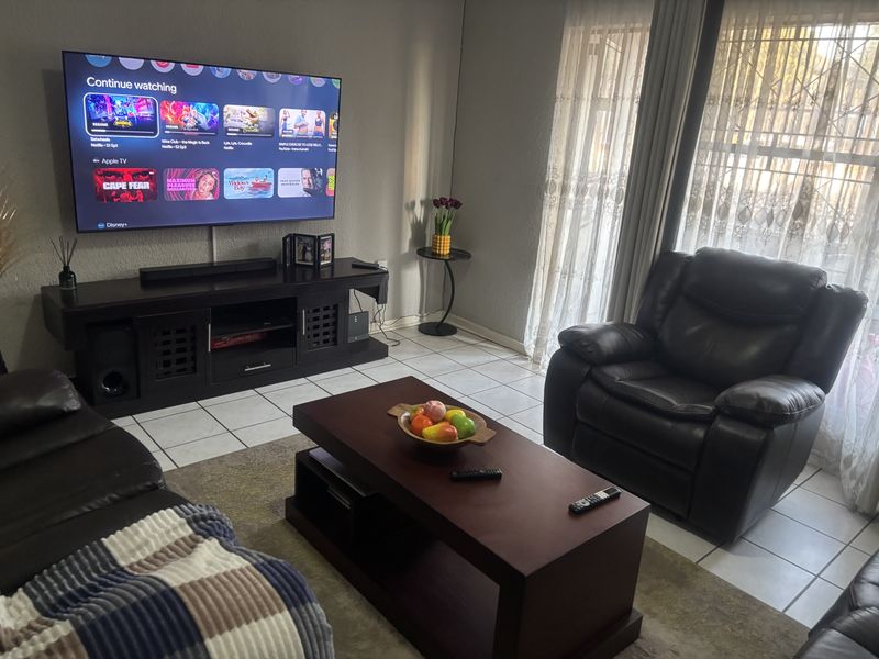 A comfortable living room featuring tiled flooring, large windows with security gates, and neutral wall finishes, providing a functional and well-lit space.