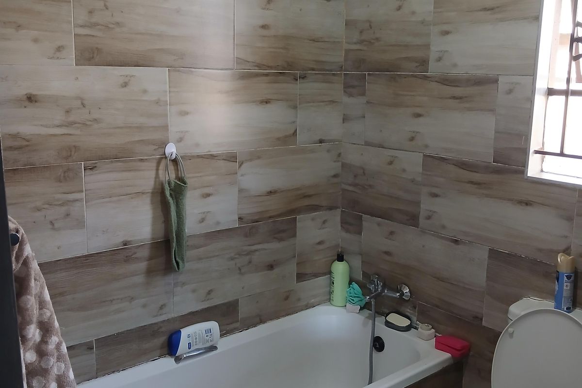 A functional bathroom featuring wood-look wall tiles, a standard bathtub, and a toilet, with natural light provided by a side window.