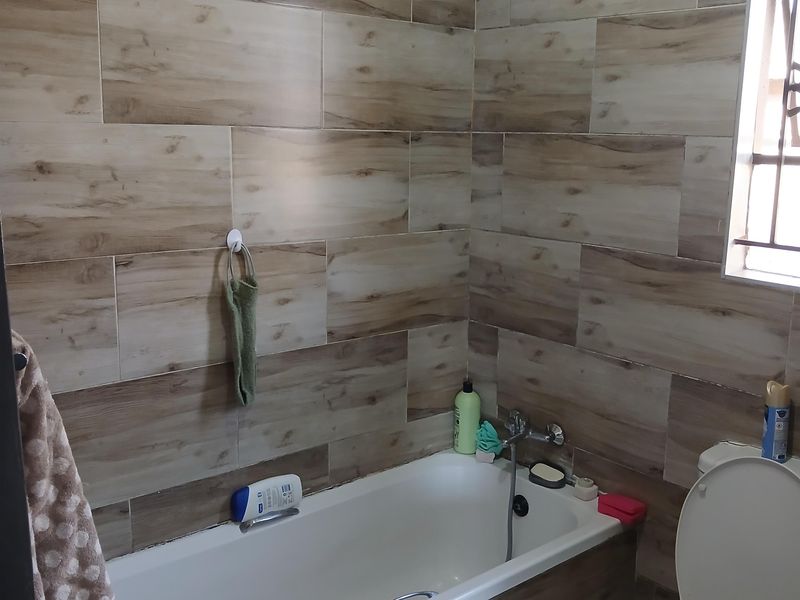 A functional bathroom featuring wood-look wall tiles, a standard bathtub, and a toilet, with natural light provided by a side window.