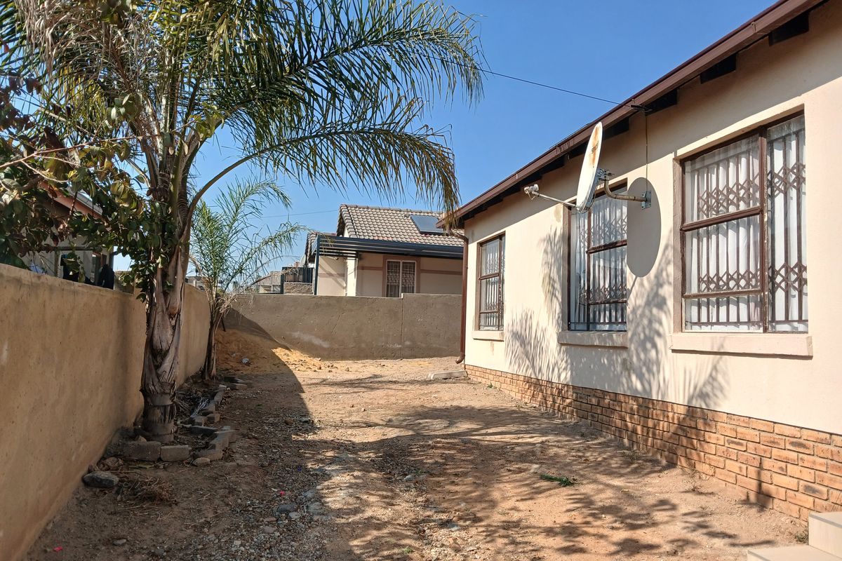 Rear exterior view of the property featuring a large, unlandscaped yard area, brick perimeter wall, and security-fitted windows.
