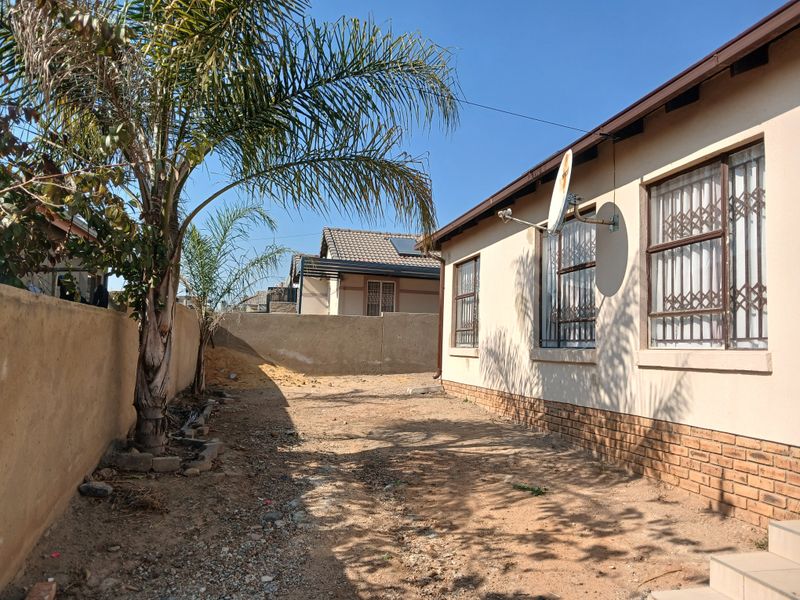 Rear exterior view of the property featuring a large, unlandscaped yard area, brick perimeter wall, and security-fitted windows.