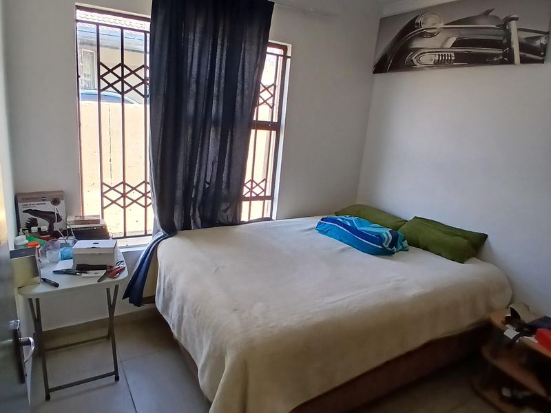 A functional bedroom featuring tiled flooring, a window with a security gate, and a central ceiling light fixture.