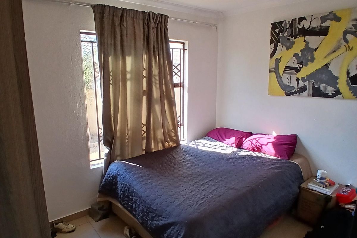 A functional bedroom featuring tiled flooring and a window fitted with security bars, providing natural light.