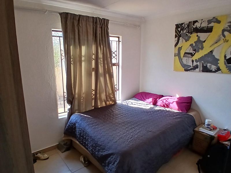 A functional bedroom featuring tiled flooring and a window fitted with security bars, providing natural light.