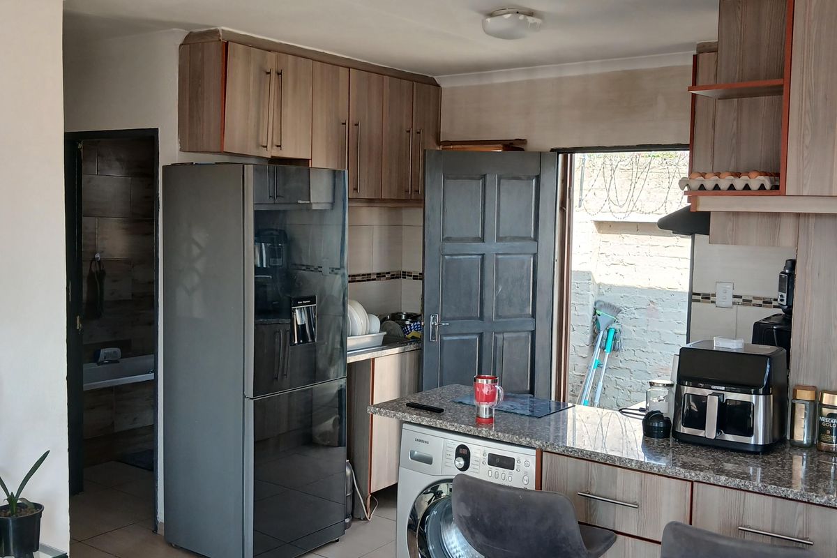Functional kitchen featuring wood-finish cabinetry, granite countertops, tiled flooring, and an integrated washing machine, with direct access to an outdoor area.