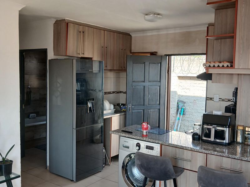 Functional kitchen featuring wood-finish cabinetry, granite countertops, tiled flooring, and an integrated washing machine, with direct access to an outdoor area.