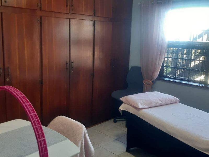 A bedroom featuring extensive built-in wooden cabinetry, tiled flooring, and a window with security bars, currently utilized as a treatment room.
