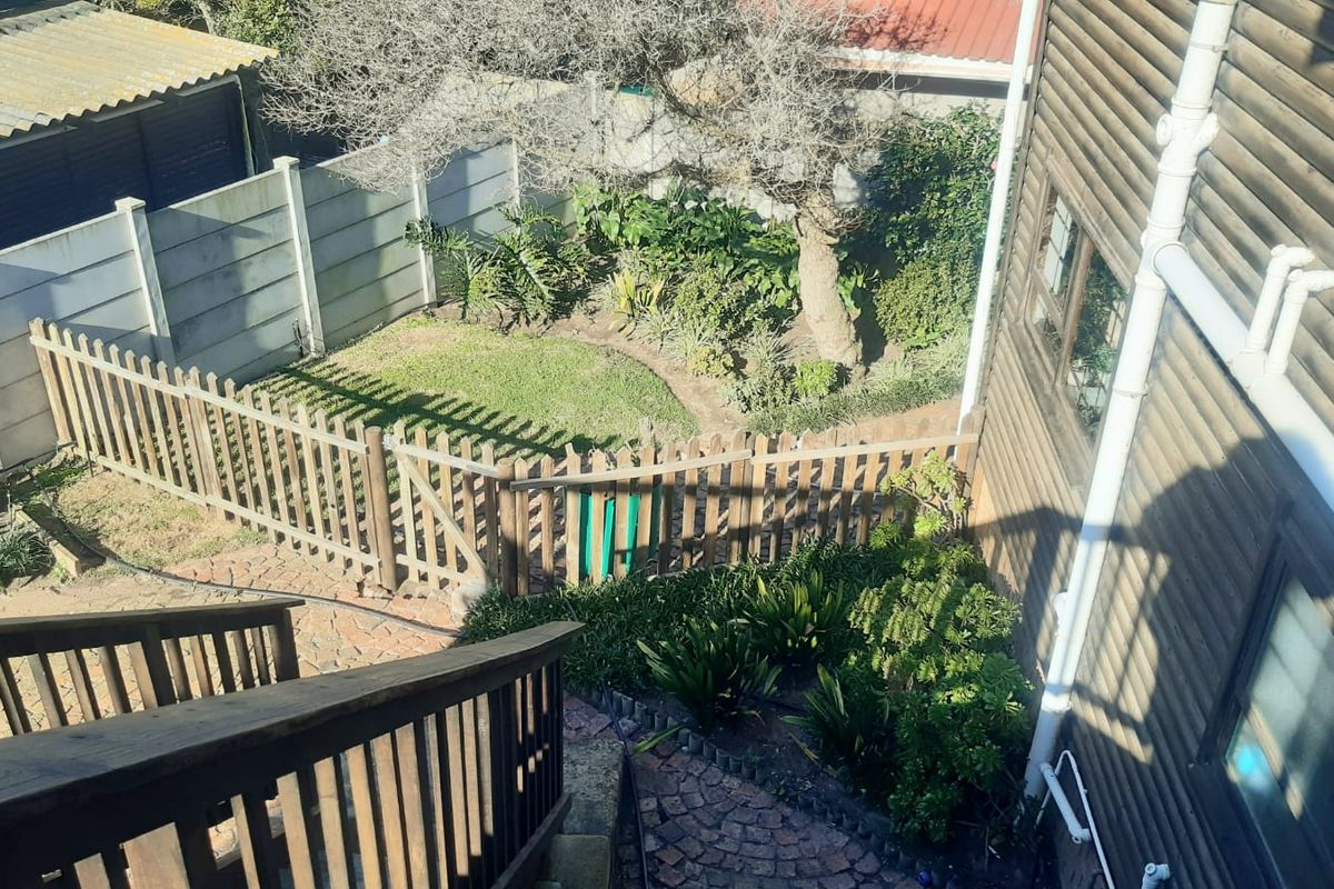 An elevated view of the rear garden featuring timber-clad exterior walls, a wooden staircase, brick paving, and a fenced lawn area.
