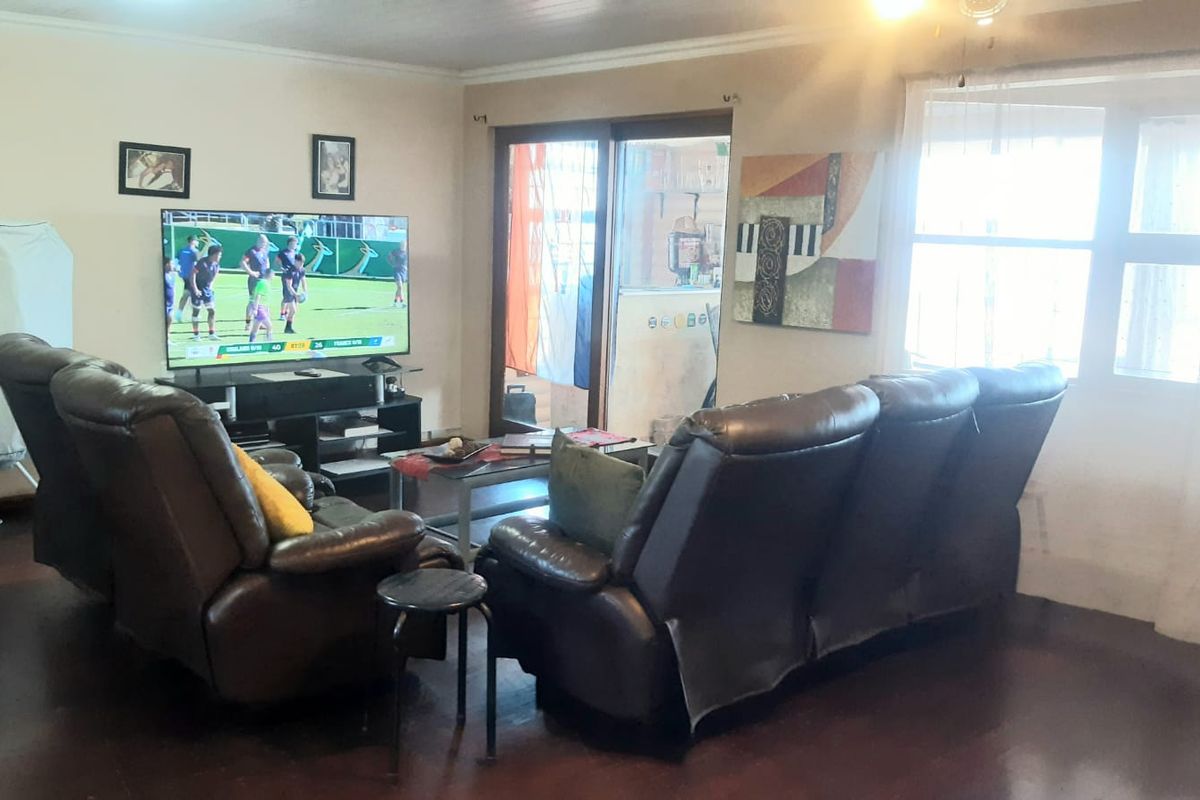 A living room featuring hardwood flooring, a large window, and a sliding glass door providing access to the exterior.