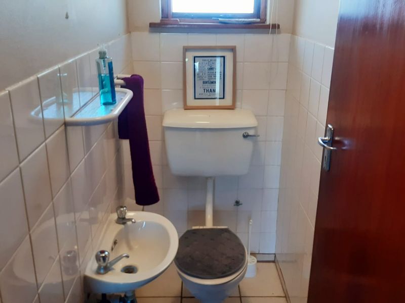 A compact guest bathroom featuring a pedestal basin, toilet, and tiled walls. The space is dated and would benefit from modern updates.