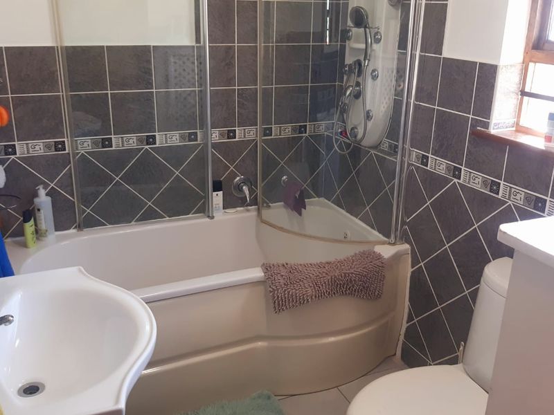 A functional bathroom featuring a bathtub with integrated shower, pedestal sink, toilet, and dark decorative wall tiling.