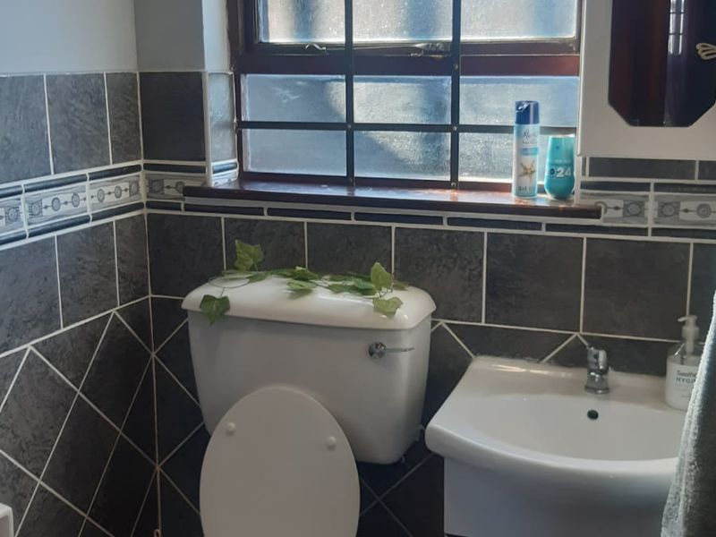 A functional bathroom featuring a vanity basin, toilet, and dark tiled walls with decorative border accents and a window with security bars.