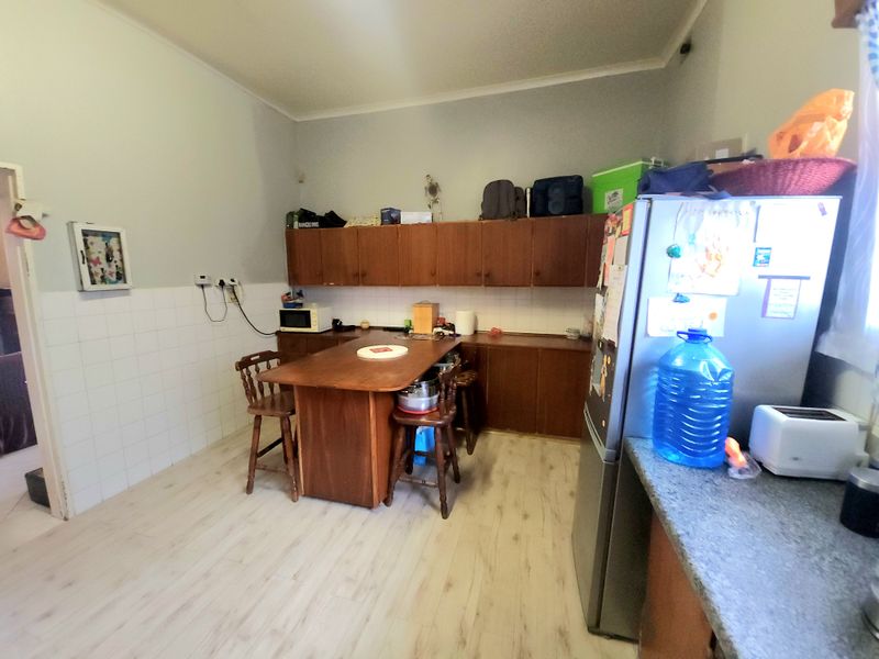 A functional kitchen featuring built-in wooden cabinetry, tiled splashbacks, and light-toned laminate flooring, offering a practical layout for daily meal preparation.