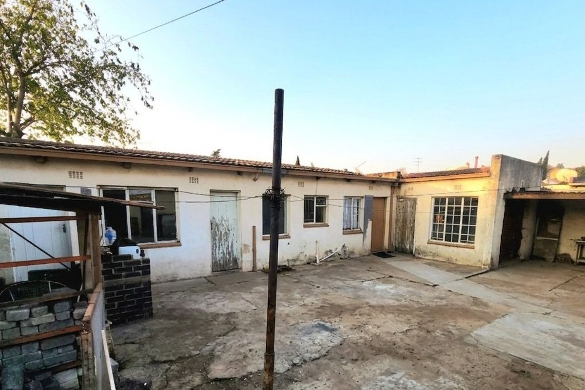 Rear exterior view of the property featuring a concrete courtyard, tiled roof, and weathered brick facade requiring maintenance and cosmetic updates.