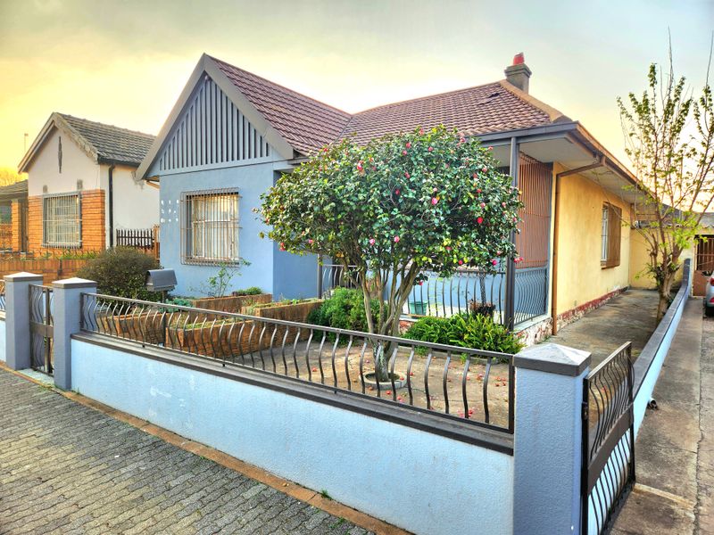 Front elevation of a single-story house featuring a tiled roof, perimeter wall with metal gate, and a covered porch area.