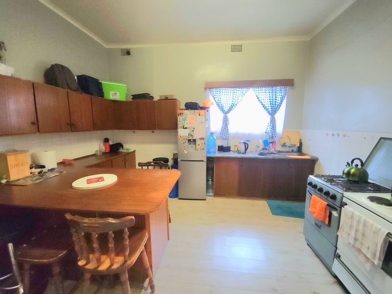 A dated kitchen featuring wood-tone cabinetry, laminate countertops, a tiled backsplash, and a freestanding stove, offering potential for a modern renovation.
