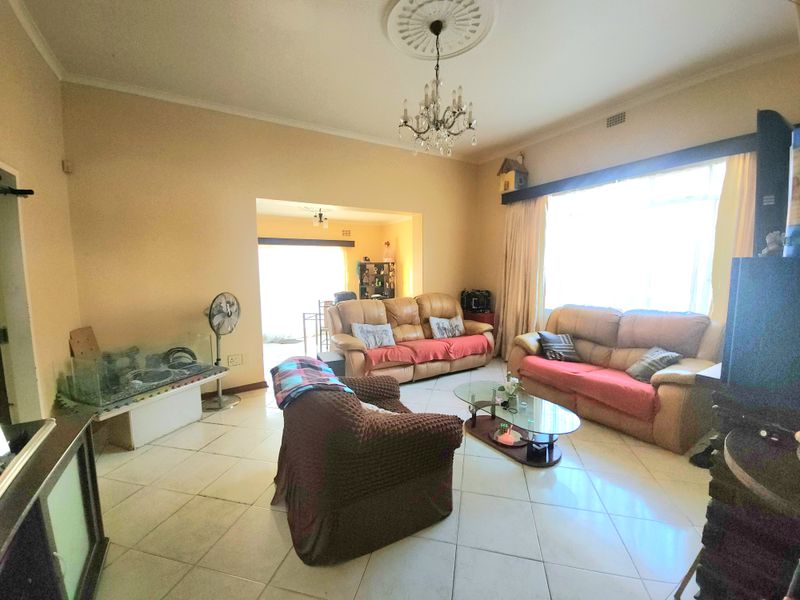 Spacious living room featuring tiled flooring, a decorative ceiling rose with a chandelier, and large windows allowing for ample natural light.