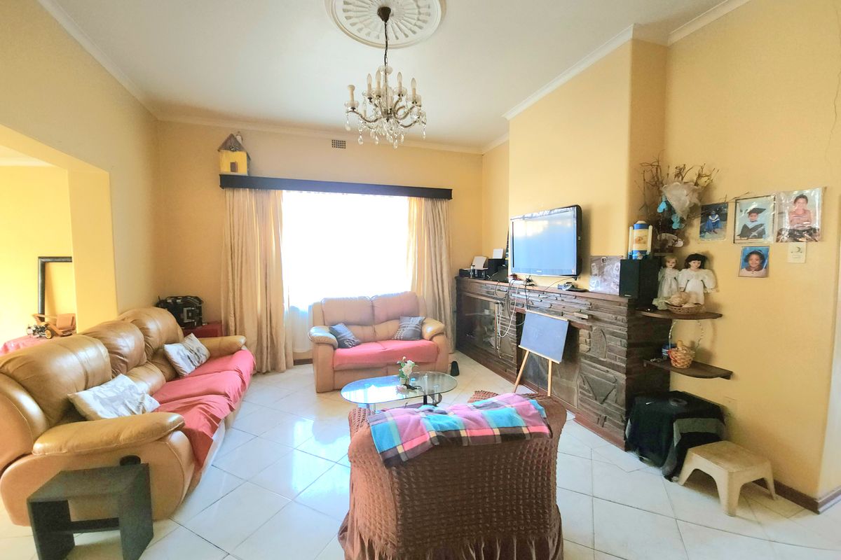 A spacious living room featuring a traditional fireplace, decorative ceiling rose with chandelier, and tiled flooring, offering a comfortable and classic living space.