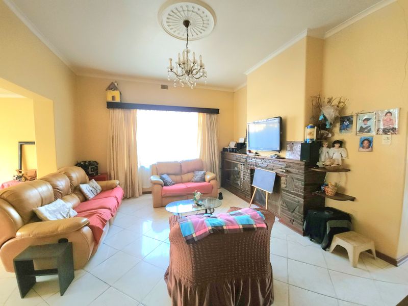 A spacious living room featuring a traditional fireplace, decorative ceiling rose with chandelier, and tiled flooring, offering a comfortable and classic living space.