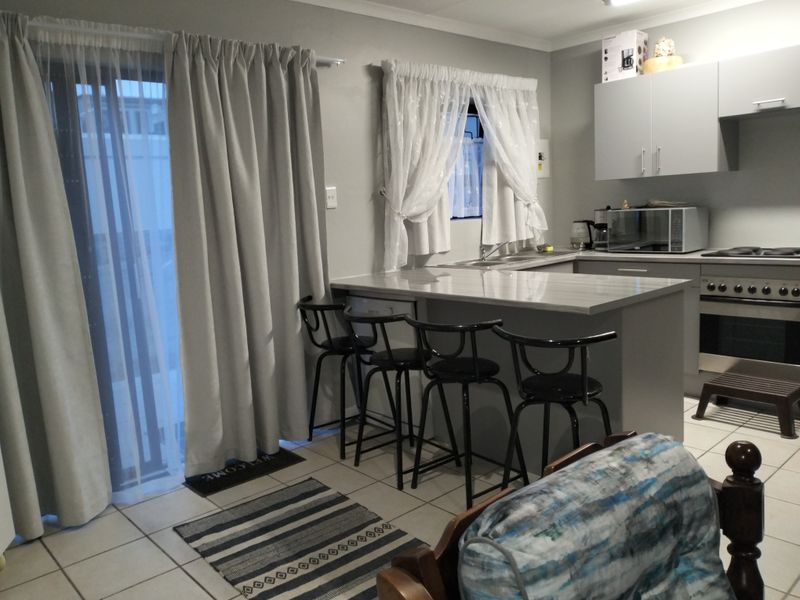 Open plan kitchen featuring modern grey cabinetry, stone-look countertops, integrated oven and hob, and direct access to the patio through a sliding glass door.