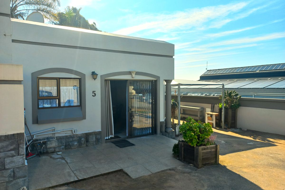 Rear exterior view of a townhouse featuring a tiled patio area, sliding glass door with security gate, and stone-clad base detailing.