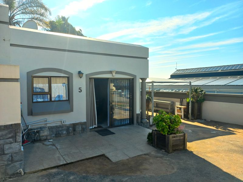 Rear exterior view of a townhouse featuring a tiled patio area, sliding glass door with security gate, and stone-clad base detailing.