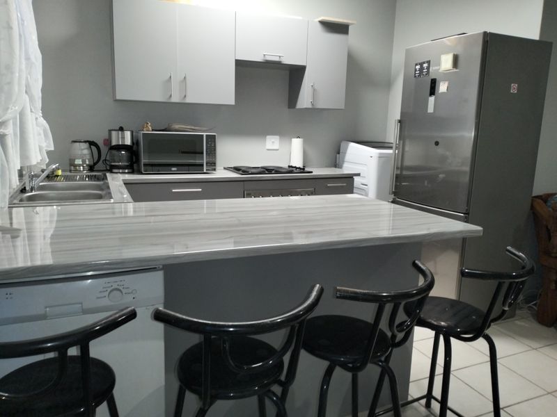 A functional kitchen featuring grey cabinetry, a breakfast bar with laminate countertop, built-in hob and oven, and tiled flooring.