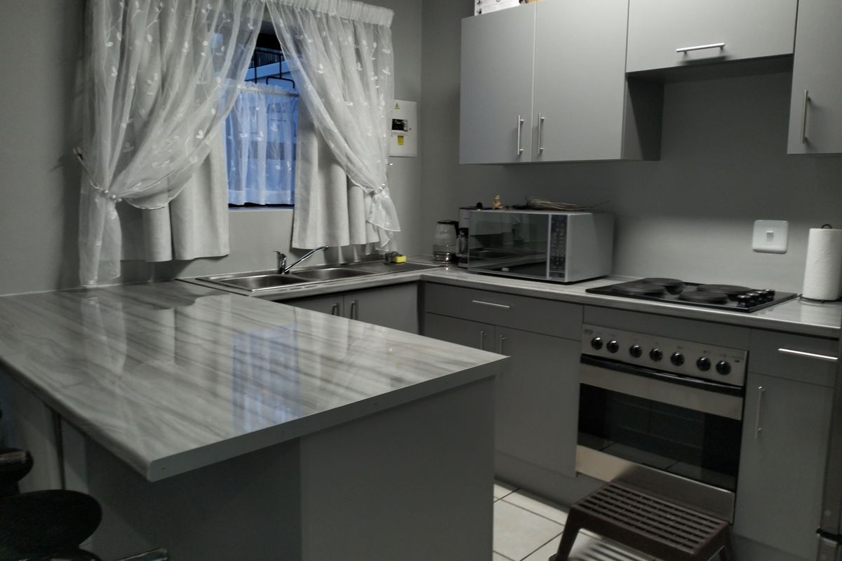 A functional kitchen featuring grey built-in cabinetry, laminate countertops, a stainless steel sink, and a built-in electric oven and stove.