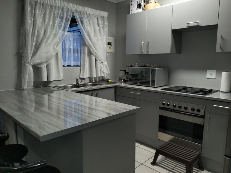 A functional kitchen featuring grey built-in cabinetry, laminate countertops, a stainless steel sink, and a built-in electric oven and stove.