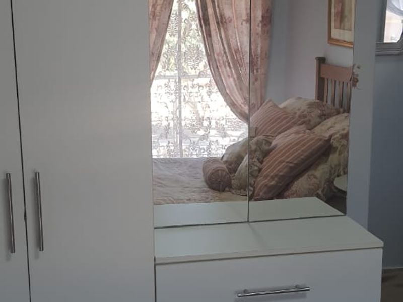 A bedroom featuring a white built-in wardrobe with an integrated vanity and mirror, complemented by tiled flooring.