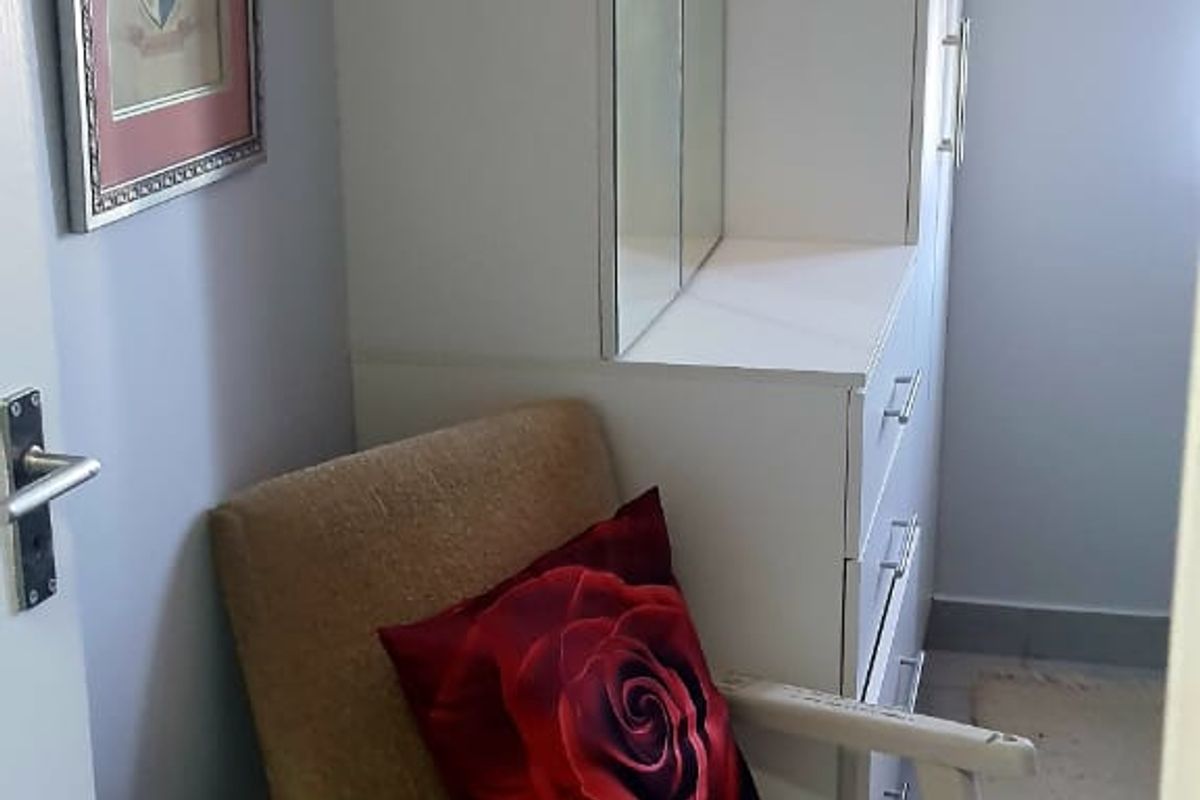 A bedroom corner featuring a white built-in wardrobe with an integrated mirrored vanity unit and neutral wall finishes.