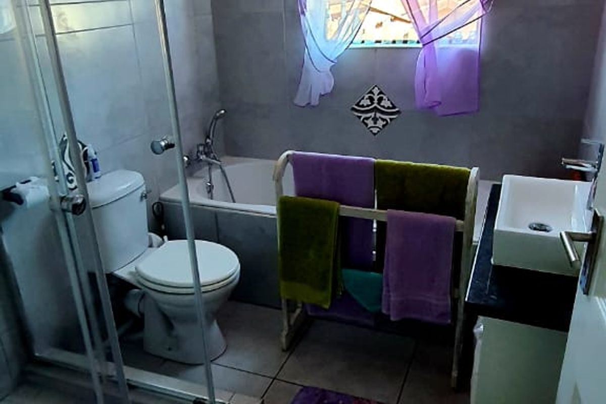 A functional bathroom featuring a glass shower enclosure, a bathtub, a toilet, and a vanity basin with neutral wall and floor tiling.
